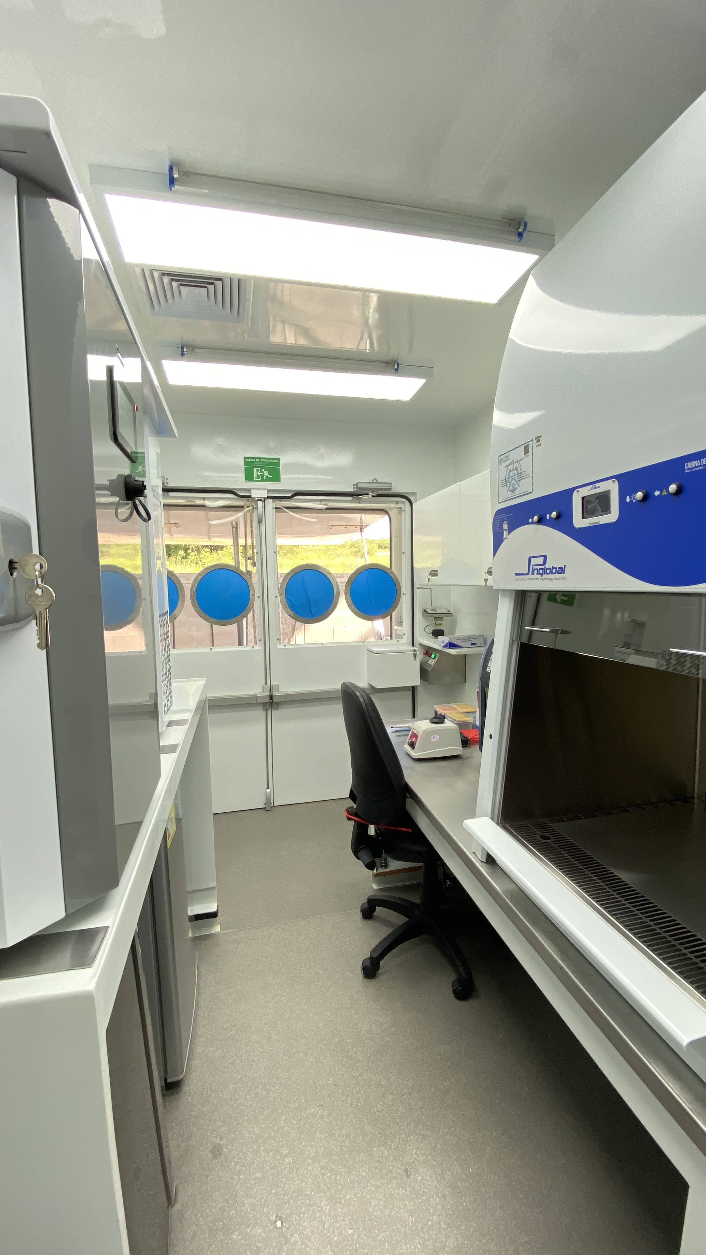 Interior of the LAB BIO MAX biological waste management area: red hazardous waste container, social distancing signage, and sample pass-through window between zones. Every element answers to a specific biosafety requirement.