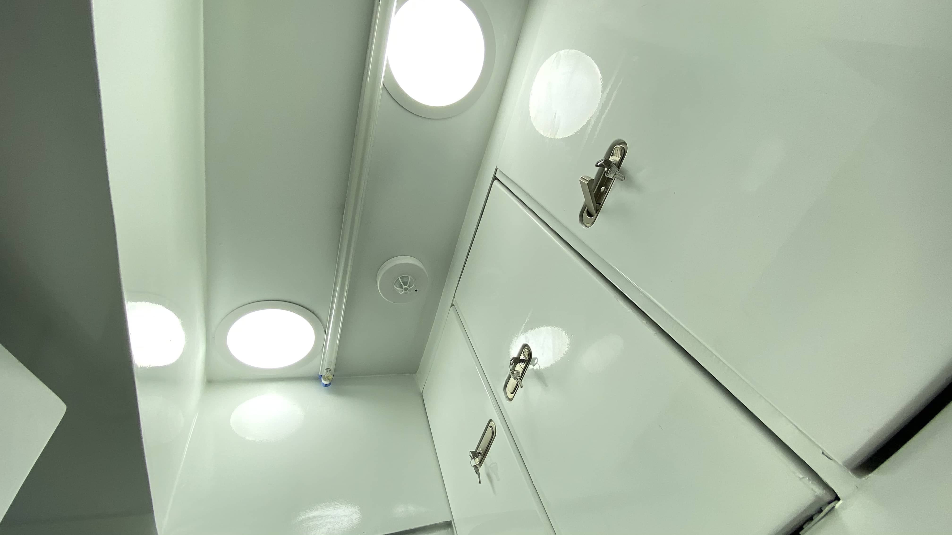 Interior module view: flush-mounted circular LED panels, germicidal UV tube, and industrial lever-lock storage cabinets. The clean geometry eliminates surfaces that are difficult to decontaminate.